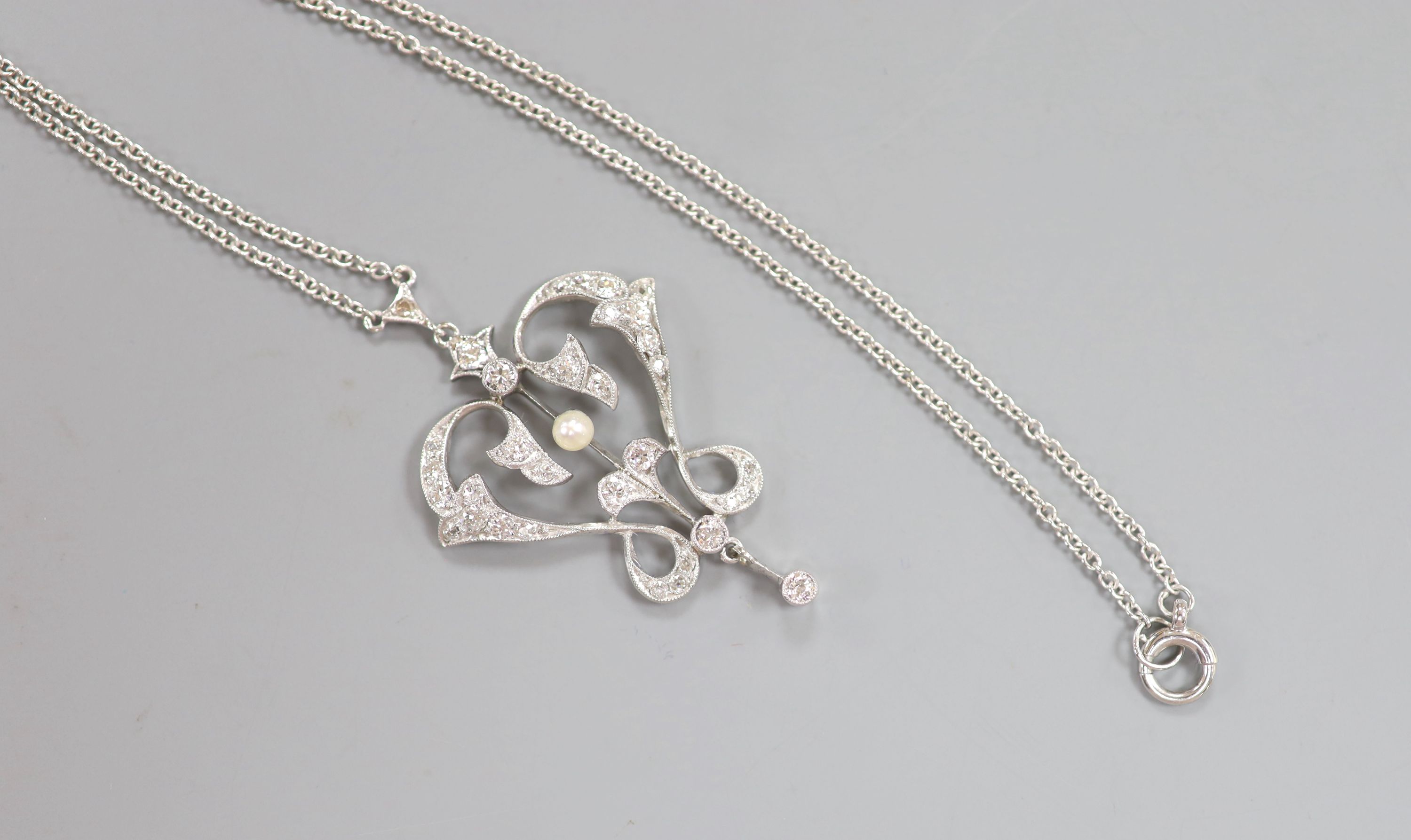 An Art Nouveau style white metal seed pearl and diamond set openwork scroll drop pendant necklace, pendant 4cm, chain 40cm,